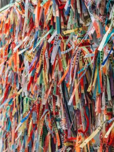 A dense mass of coloured cloth ribbons tied to a rail, layered over one another.