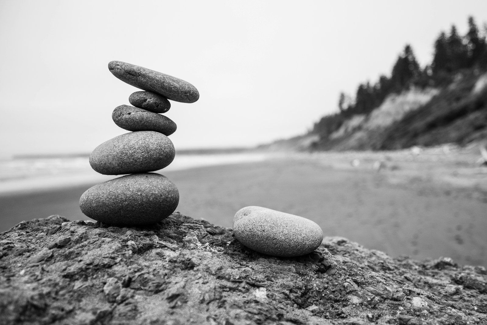 Black and white photograph of small flat stones balanced in a stack on a stony beach.