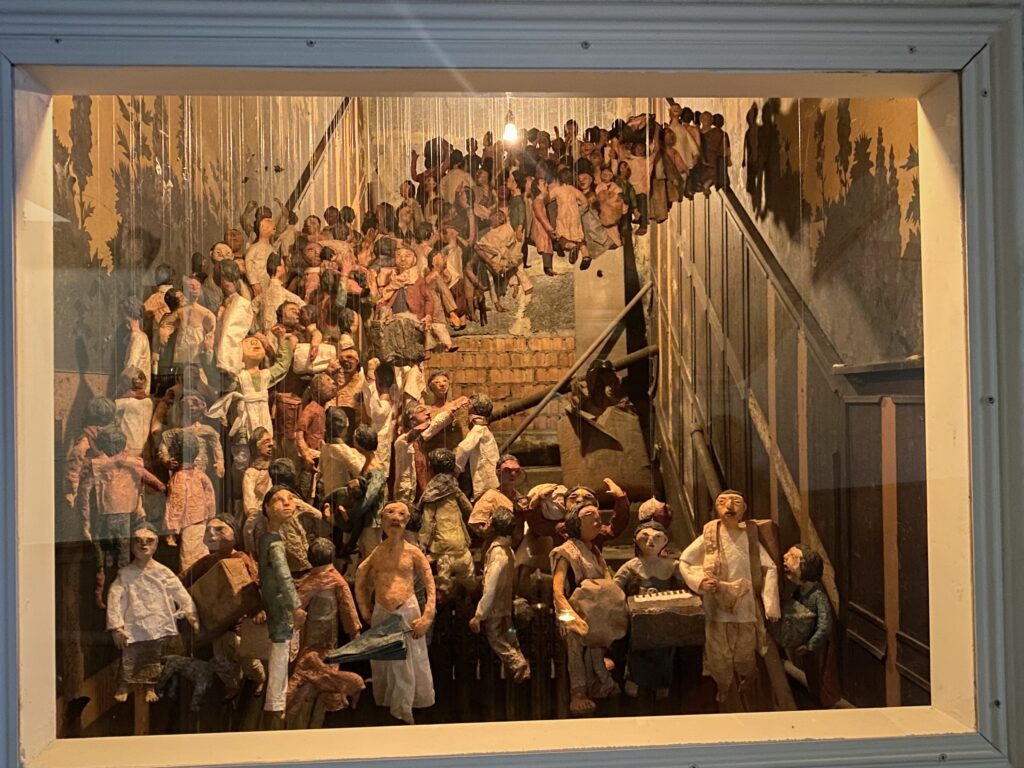 A large framed painting of a crowd of figures, hung on a wall.