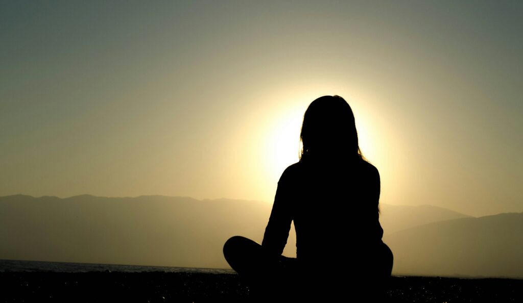 A person sitting cross-legged on a hilltop with the ground falling away, one of the two dimensions of growth without the other.