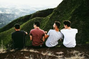 Men and Emotions: Why It’s So Hard to Talk Alex Golding Therapy Four men sitting side by side on a steep green hillside, looking out over the valley.