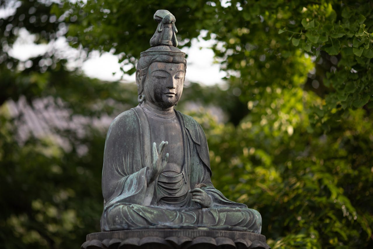 A weathered stone Buddha seated in meditation, surrounded by foliage.