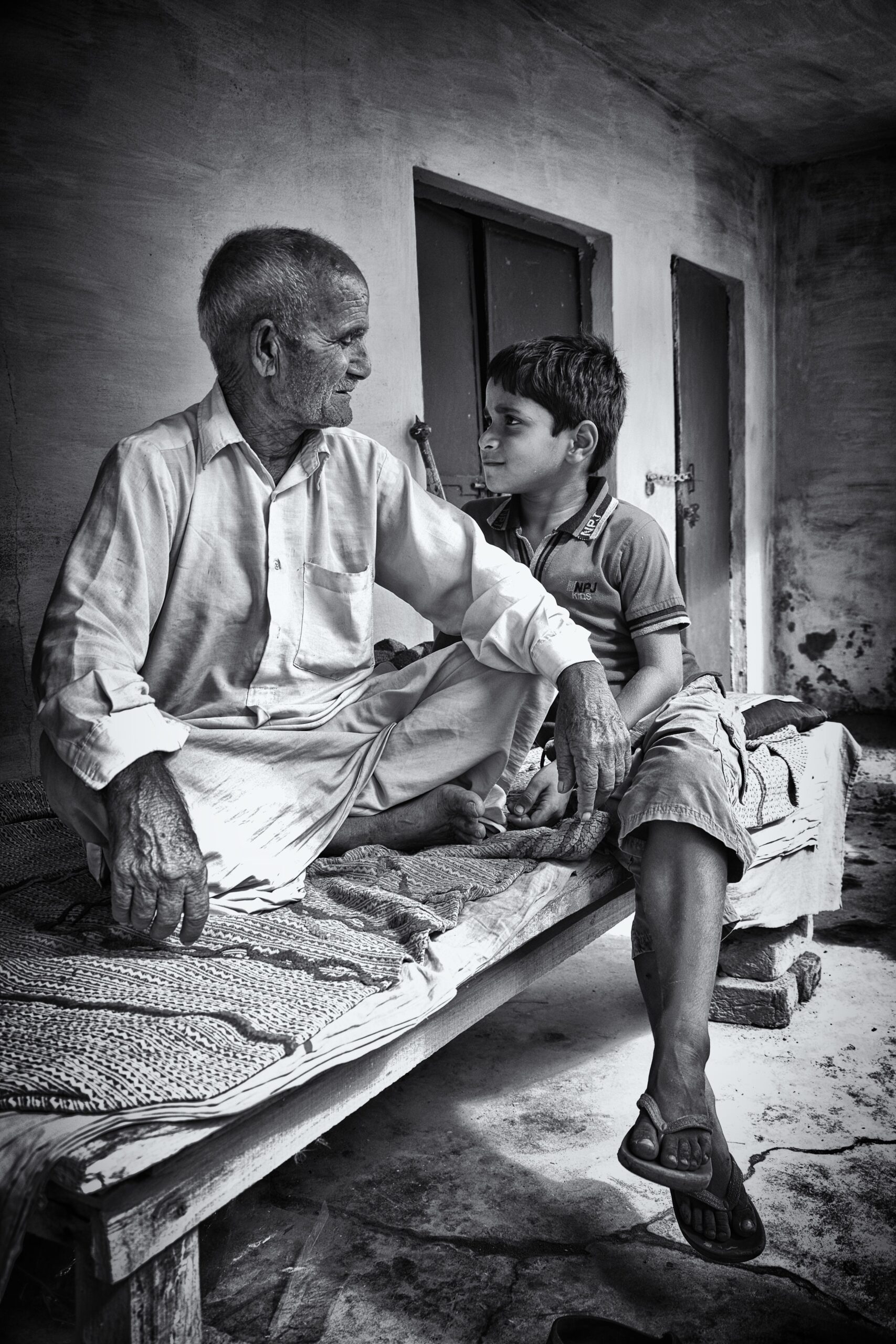 An older man and a boy sitting together outside a house, turned towards each other in conversation