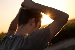 Psychosynthesis Therapy for Anxiety & the Inner Critic Alex Golding Therapy A man standing against a low sun with both hands raised to the back of his head.