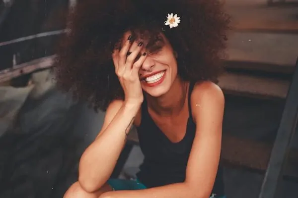 Conscious Kindness: A Compassionate Response to the Harsh Inner Critic Alex Golding Therapy A woman with dark curly hair sitting quietly with one hand resting against her face.