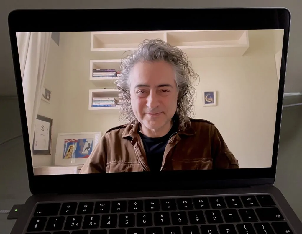 A laptop open on a desk, showing Alex Golding on a video call.