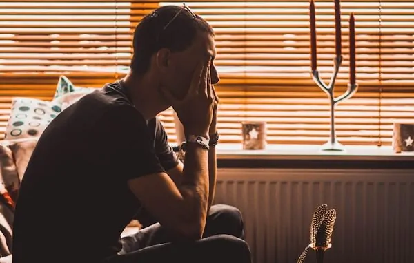 All Spirit, No Ground. All Ground, No Meaning. Alex Golding Therapy A person sitting on the floor at home, leaning back against a radiator with one hand in their hair.