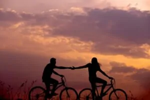 Love, Loss & the Art of Intimacy Alex Golding Therapy Two people on bicycles ride towards the sunset