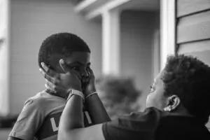 Conscious Kindness: A Compassionate Response to the Harsh Inner Critic Alex Golding Therapy Black and white photograph of two children, one leaning in to whisper to the other.