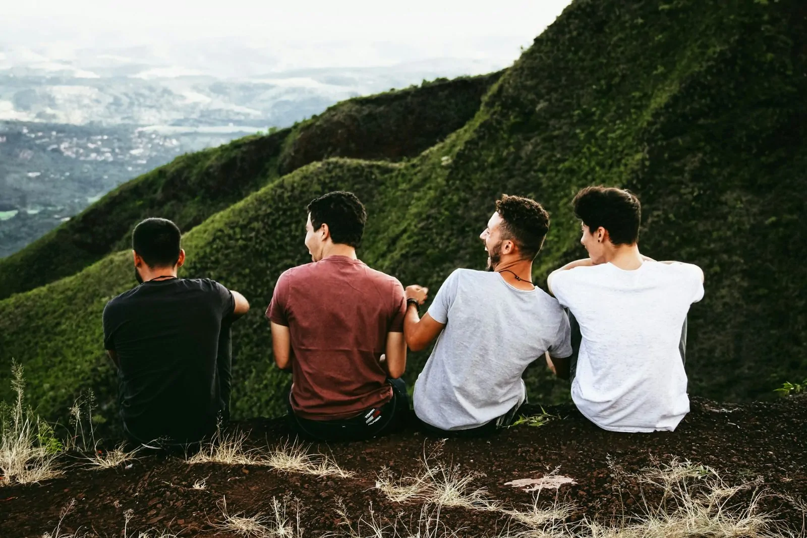Four men sitting side by side on a steep green hillside, looking out over the valley.