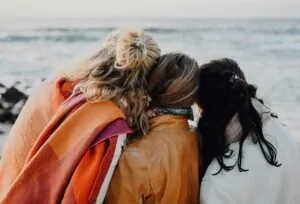 Two people seen from behind, wrapped in a blanket with their heads together.