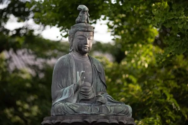 From Crisis to Calling: Psychosynthesis Therapy for Meaningful Life Transitions Alex Golding Therapy A weathered stone Buddha seated in meditation, surrounded by foliage.
