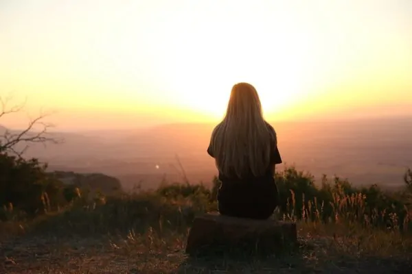 Buddhist Therapy London: Mindfulness Counselling & the Spiritual Approach Alex Golding Therapy A person sitting alone on high ground, looking out over hills as the sun comes up.